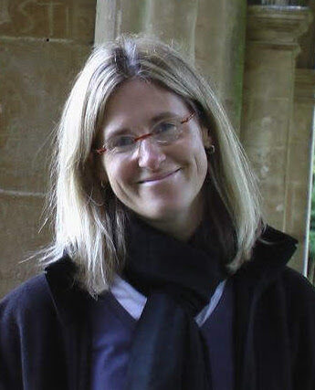 A photo of a smiling woman wearing glasses and standing outside in an archway.