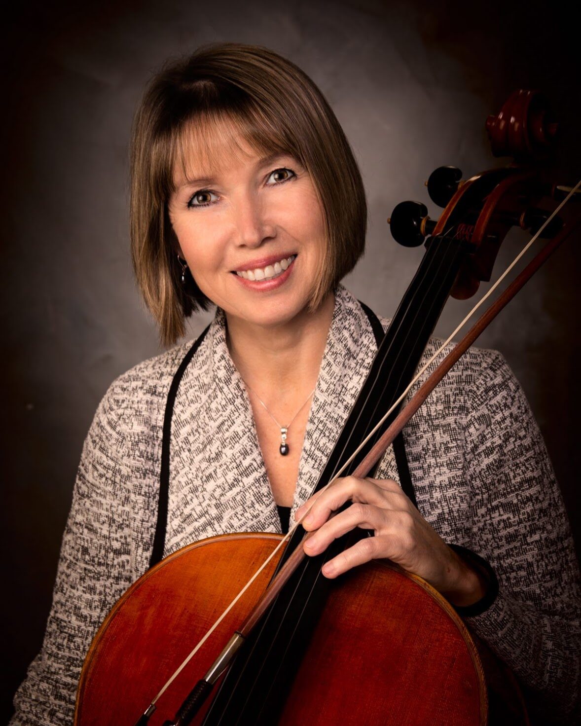 A smiling woman with a bob haircut holds her cello.