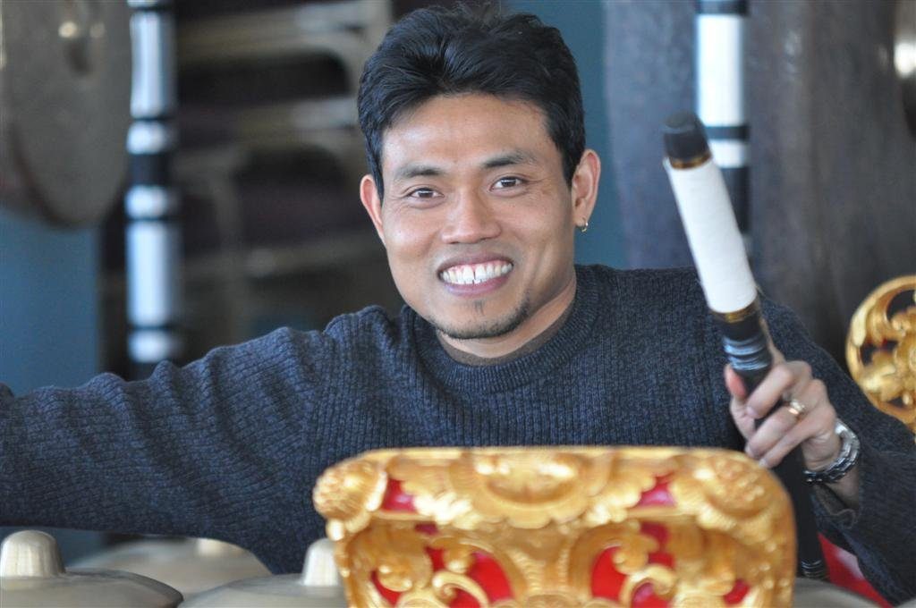 smiling gamelan teacher with red and gold instrument 