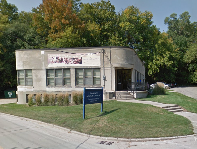A photo of a building among the trees. A banner is hung on the building that says "Sharing the joy of music-making since 1874." The sign in front says "Lawrence Academy of Music - Lawrence University."