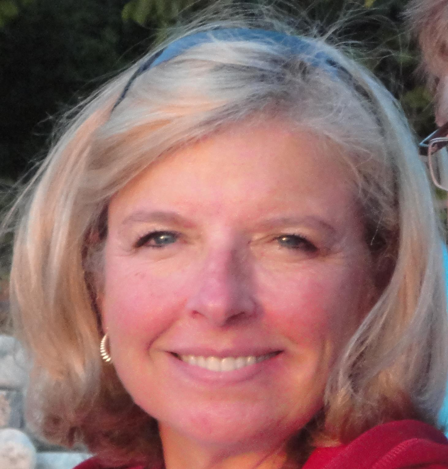 A headshot of a smiling woman with a blond bob and wearing a headband and earrings.