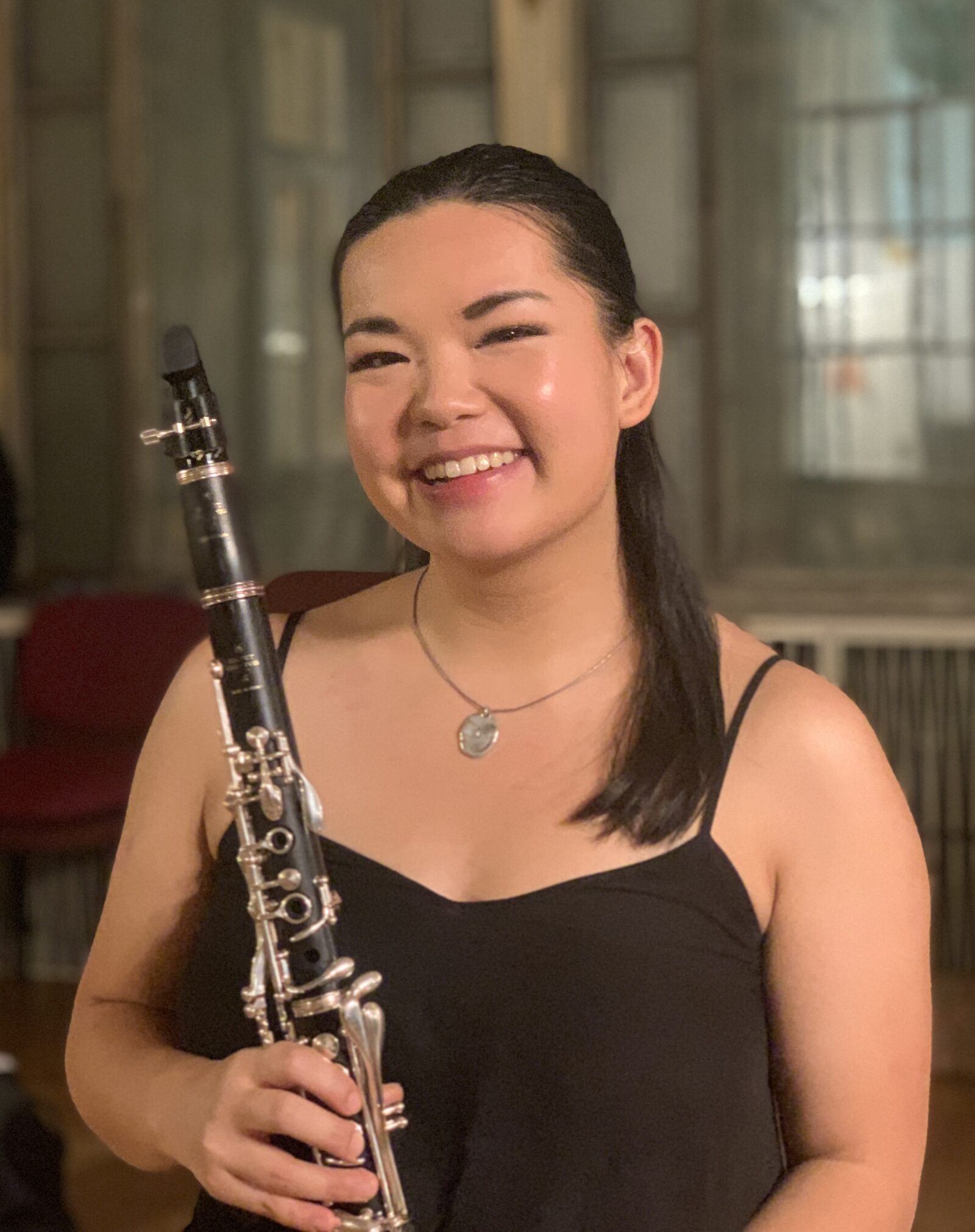 A headshot of a smiling woman in concert black holding a clarinet.
