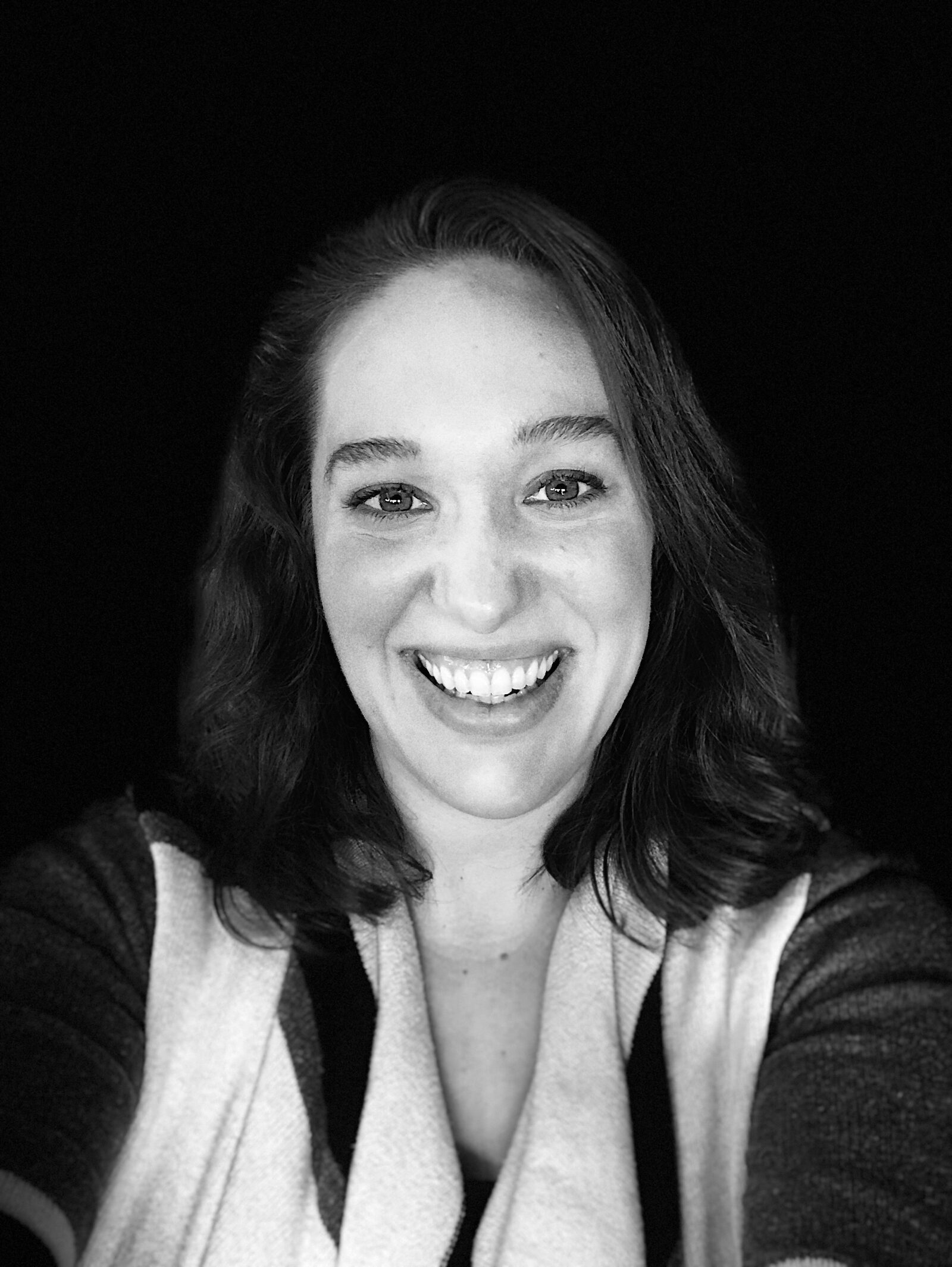 A black and white headshot of a smiling woman with shoulder-length, wavy hair.